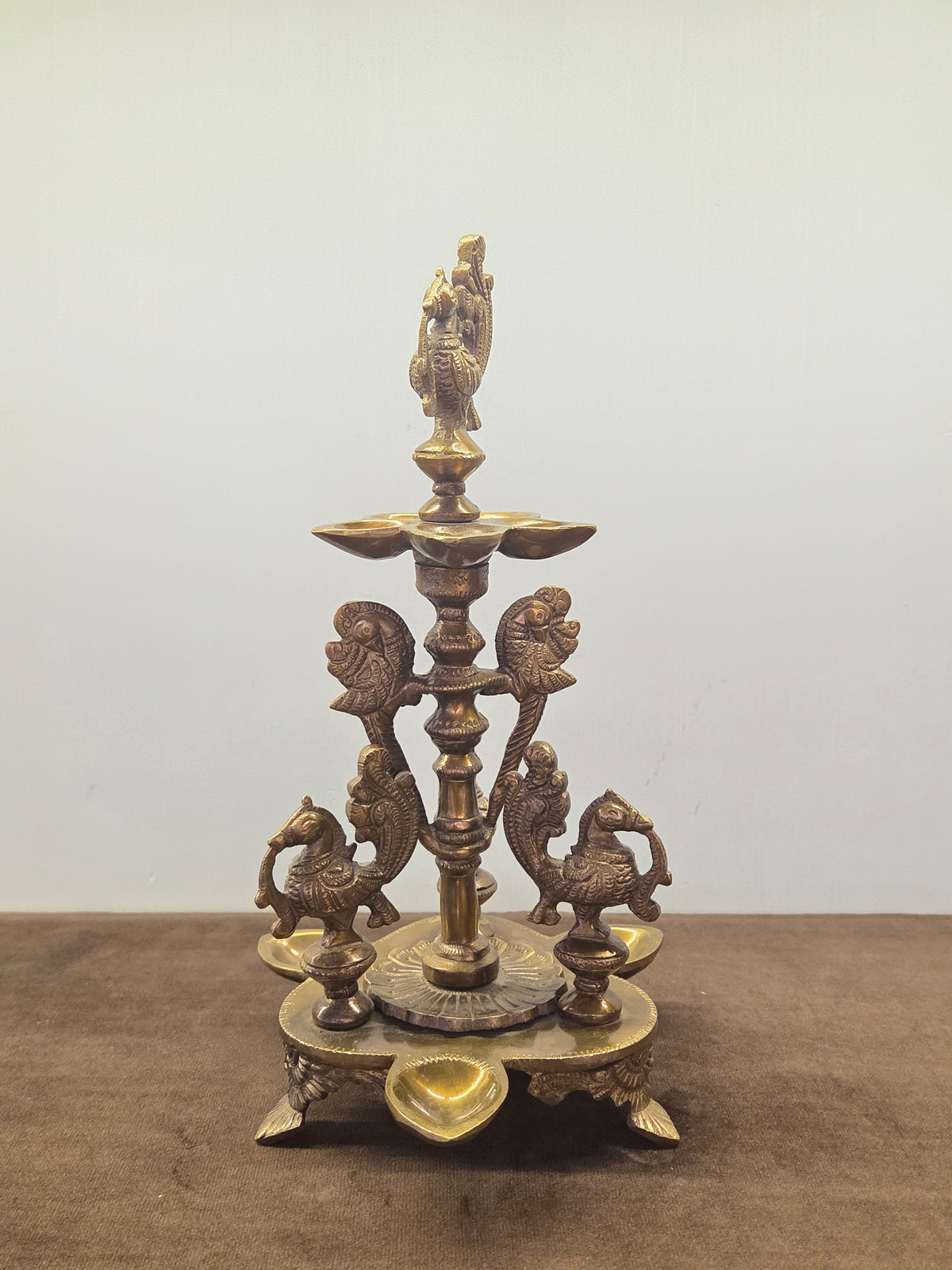 Antique brass peacock diya with four cast birds on a turned column, a lobed pan and wells in the base - Peetal Parampara