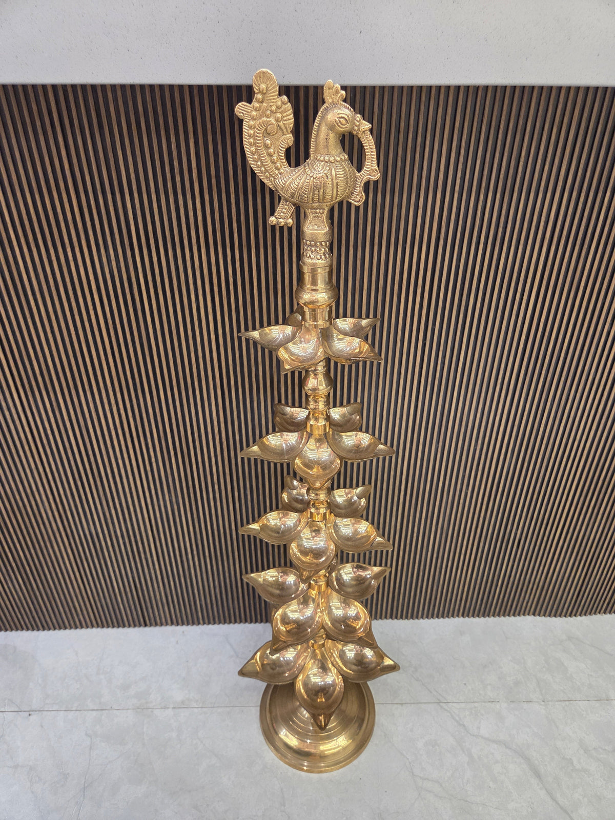 Polished brass layered diya with five tiers of pointed oil cups on a turned stem under a cast peacock - Peetal Parampara