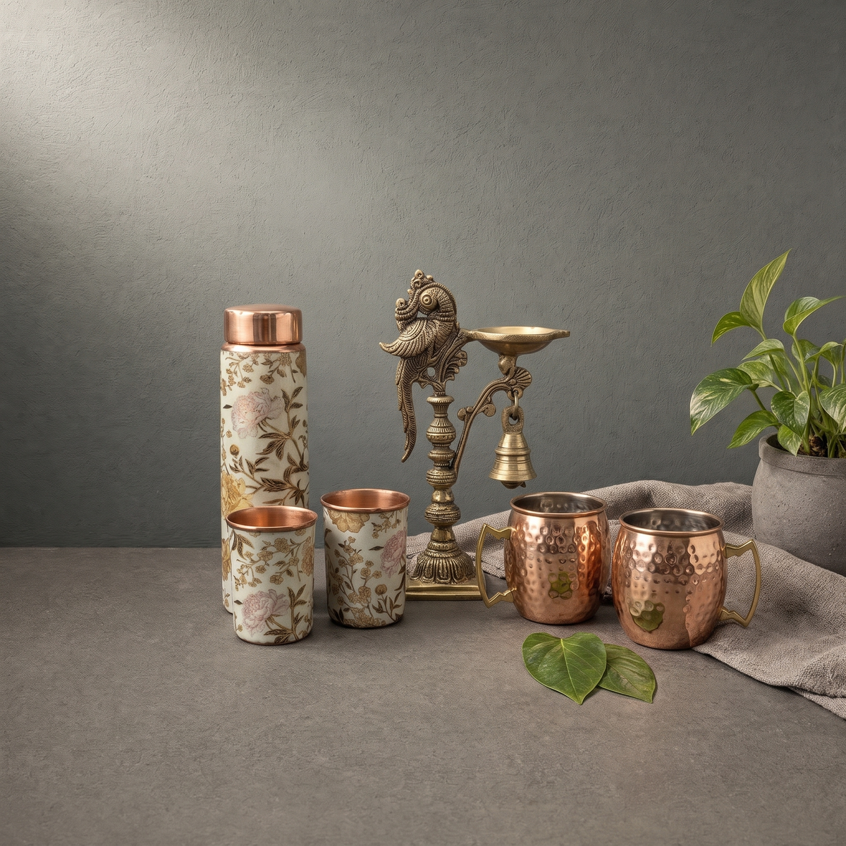 Antique Brass Parrot Diya with Bell, Copper Floral Bottle and Tumbler Set on a stone ledge - Peetal Parampara