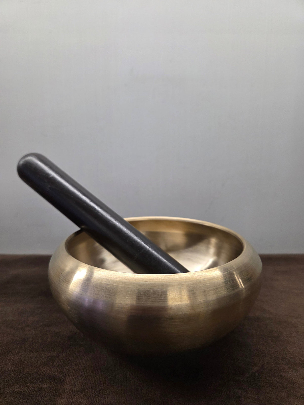 Turned kansa massage bowl with an inturned rim and a plain dark wand resting across it - Peetal Parampara