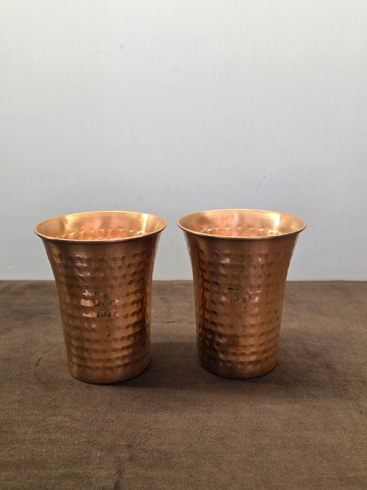 Two flared copper tumblers hammered in oval facets, narrow at the base and rolled over at the wide lip - Peetal Parampara