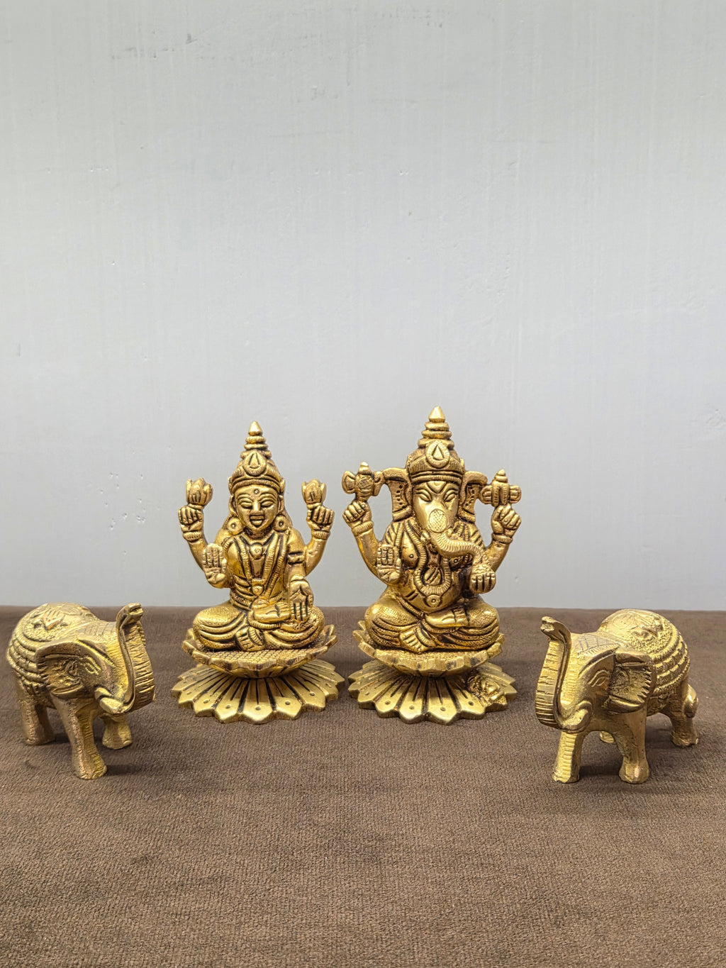 Brass Laxmi and Ganesh murtis on flat lotus bases with a brass elephant at either end, trunks raised - Peetal Parampara