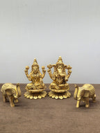 Brass Laxmi and Ganesh murtis on flat lotus bases with a brass elephant at either end, trunks raised - Peetal Parampara