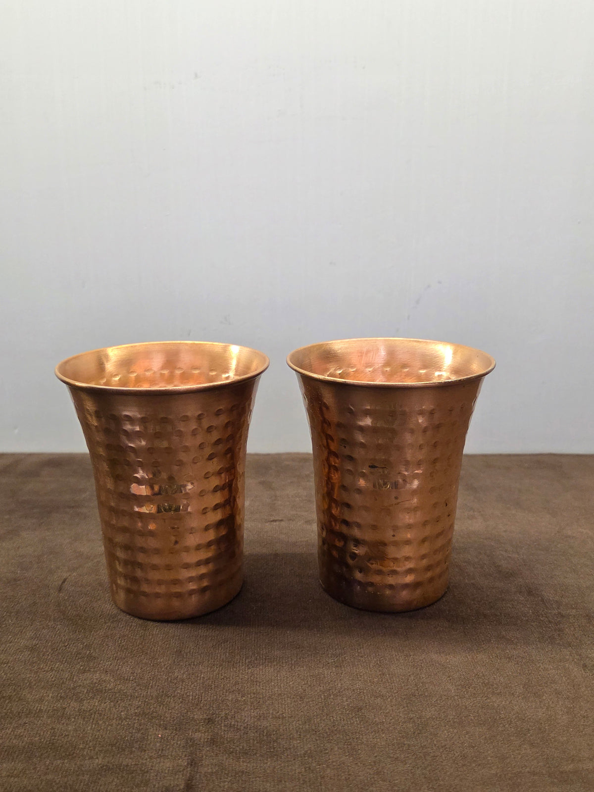 Two flared copper tumblers hammered in oval facets, narrow at the base and rolled over at the wide lip - Peetal Parampara