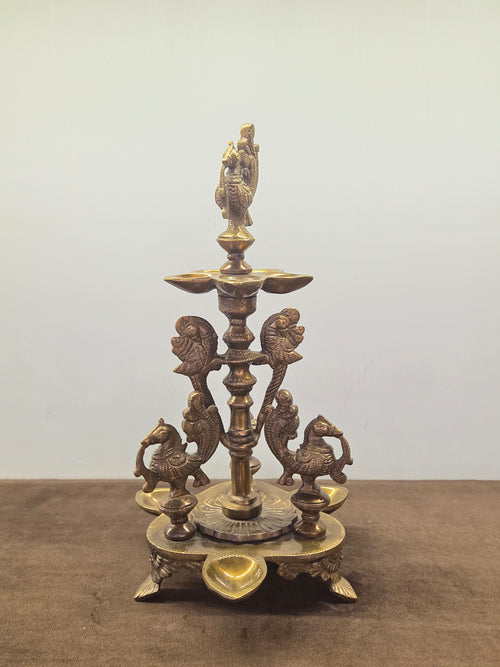 Antique brass peacock diya with four cast birds on a turned column, a lobed pan and wells in the base - Peetal Parampara