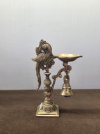 Cast brass parrot diya with an oval oil pan on a side arm, a bell below it and a square stepped base - Peetal Parampara