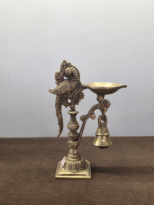 Cast brass parrot diya with an oval oil pan on a side arm, a bell below it and a square stepped base - Peetal Parampara