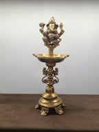 Antique brass standing lamp with a seated four-armed Ganesh over a lobed oil bowl, on four cast feet - Peetal Parampara