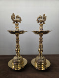 Pair of polished brass standing lamps with cast peacock finials, spouted oil pans and fluted bell feet - Peetal Parampara