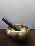 Turned kansa massage bowl with an inturned rim and a plain dark wand resting across it - Peetal Parampara