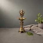 Antique Brass Ganesh Standing Diya on a stone ledge against a grey plaster wall - Peetal Parampara
