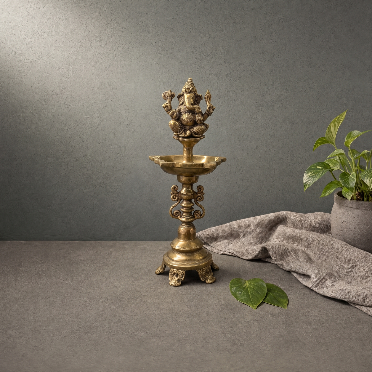 Antique Brass Ganesh Standing Diya on a stone ledge against a grey plaster wall - Peetal Parampara