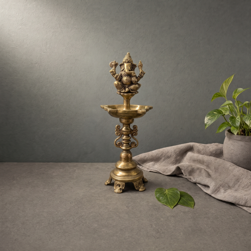 Antique Brass Ganesh Standing Diya on a stone ledge against a grey plaster wall - Peetal Parampara