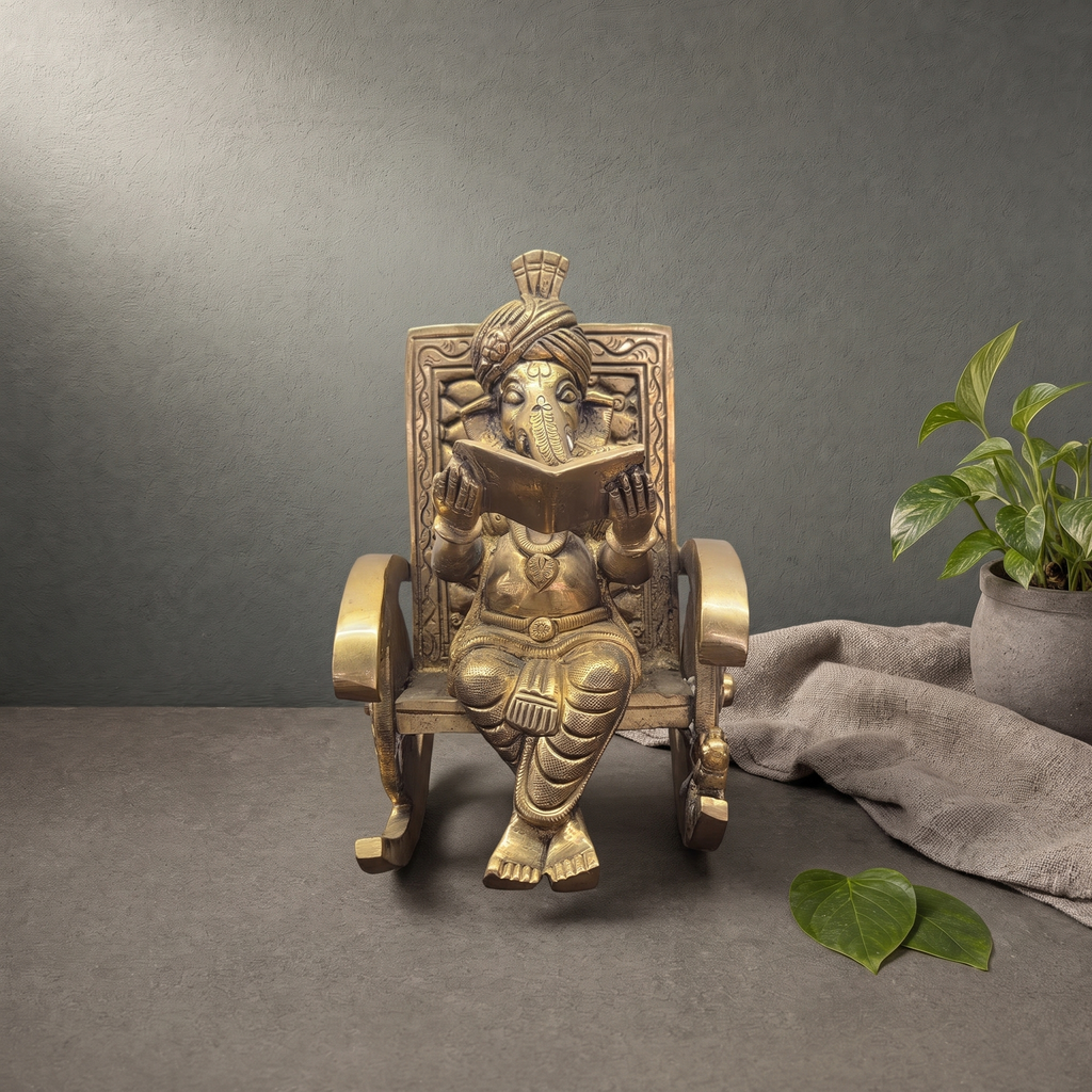 Brass Ganesh Murti in a Rocking Chair on a stone ledge against a grey plaster wall - Peetal Parampara