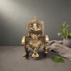 Brass Ganesh Murti in a Rocking Chair on a stone ledge against a grey plaster wall - Peetal Parampara