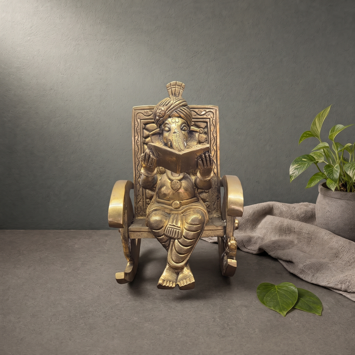 Brass Ganesh Murti in a Rocking Chair on a stone ledge against a grey plaster wall - Peetal Parampara