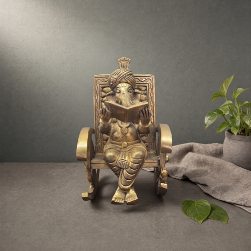 Brass Ganesh Murti in a Rocking Chair on a stone ledge against a grey plaster wall - Peetal Parampara
