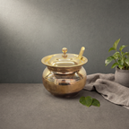 Brass Ghee Pot with Spoon on a stone ledge against a grey plaster wall - Peetal Parampara