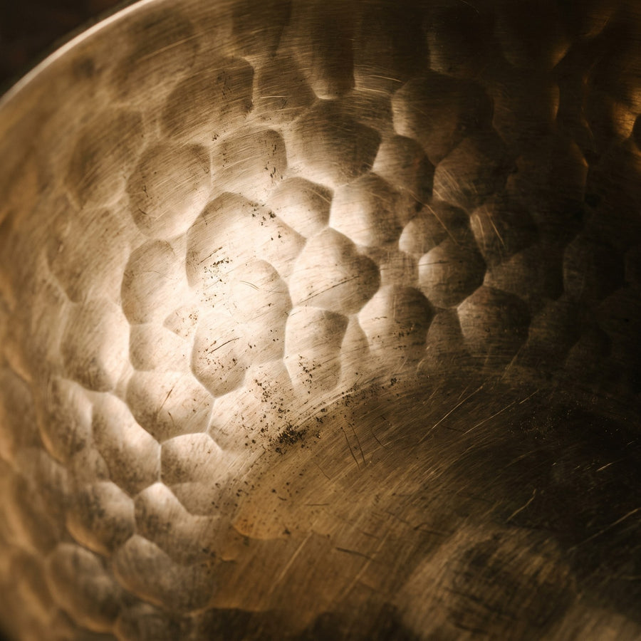 Close view of a hammered brass surface, the facets differing in size and spacing and each catching the light at its own angle.