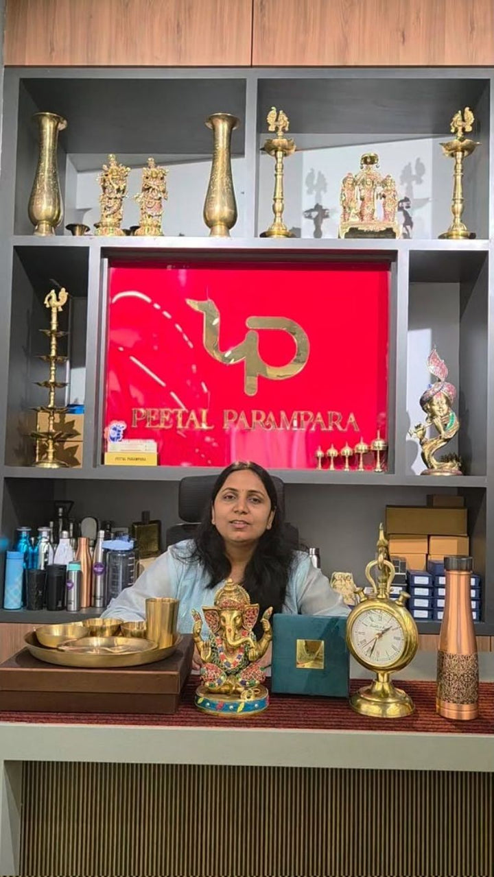 A wall of shelves holding brass diyas, murtis and vessels, with the Peetal Parampara sign on the panel behind.