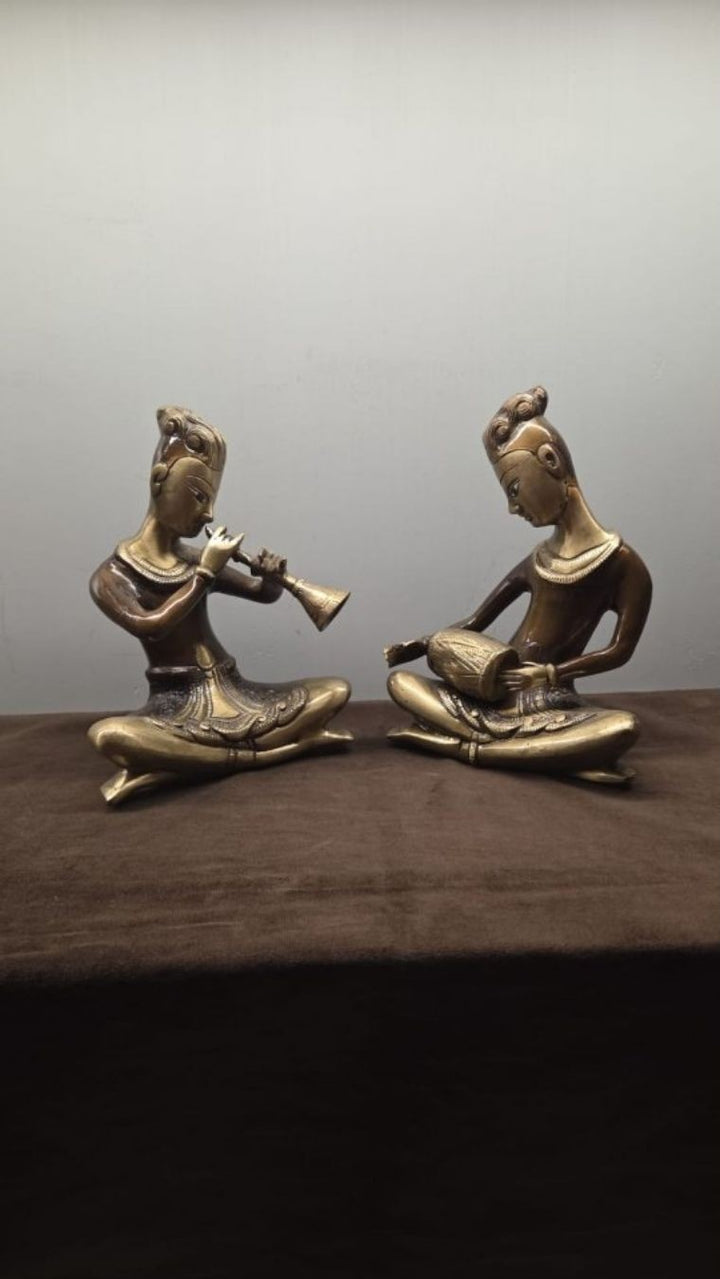 Two brass figures seated facing one another on a dark wooden surface, each playing an instrument.