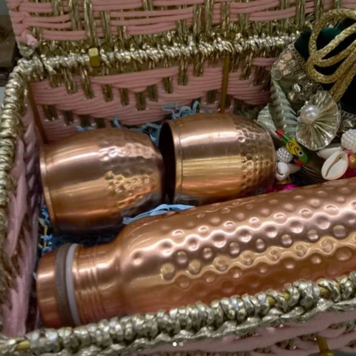 Copper vessels with hammered bodies lying in an open gift box, beside strings of small white flowers.