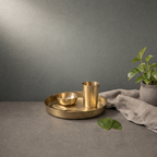 Kansa Baby Thali Set on a stone ledge against a grey plaster wall - Peetal Parampara