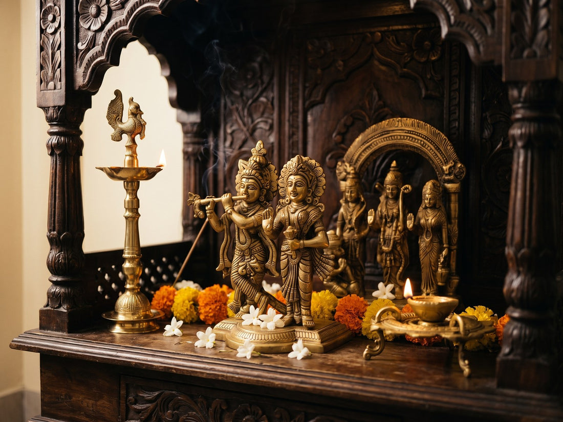 A carved wooden home mandir holding brass murtis, with a standing brass diya lit beside them and marigold and jasmine laid along the ledge.